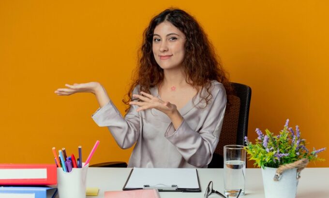 pleased-young-pretty-female-office-worker-sitting-desk-with-office-tools-points-with-hands-side-isolated-orange_141793-73519 pleased-young-pretty-female-office-worker-sitting-desk-with-office-tools-points-with-hands-side-isolated-orange_141793-73519